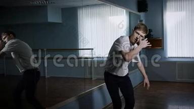 嘻哈舞者站在舞蹈工作室的镜子附近表演他的舞蹈。 年轻人的流畅的动作。