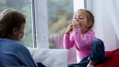 兄妹俩坐在窗台上，吃着苹果，看着窗外。
