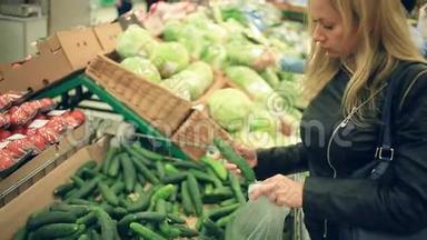 一个女人在<strong>蔬菜</strong>货架上的<strong>超市</strong>里买<strong>蔬菜</strong>和<strong>水果</strong>。 男人选黄瓜