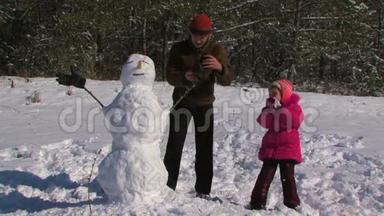 爸爸和小女儿在森林附近的草地上堆雪人..