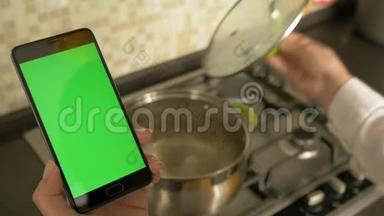 一个女人拿着一台绿色屏幕的智能手机，煮汤。