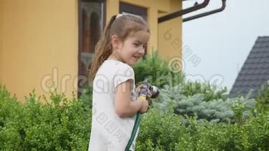 可爱的小女孩拿着一根水管，在给草坪浇水时摇动它