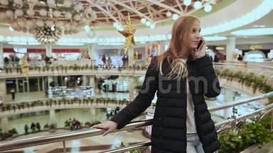 穿着夹克的可爱的年轻女孩，用手机说话，结束了在一个大购物中心的电话。