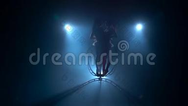 空中杂技演员女孩在空中优雅地旋转一个金属环。 <strong>黑烟</strong>背景。 剪影。 慢动作