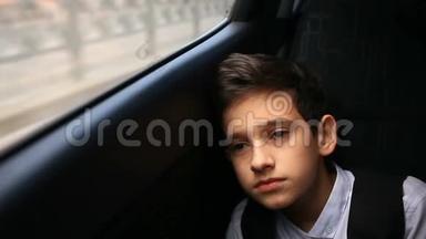 少年坐在车里看着窗外。 窗外闪烁着城市的树木和房屋