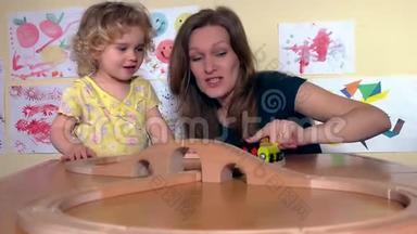 快乐的保姆和幼儿女孩在幼儿园玩木火车