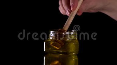 蜂蜜从黑色背景的蜂蜜勺上滴下。健康的有机浓蜂蜜，从木制的蜜匙中蘸取。。