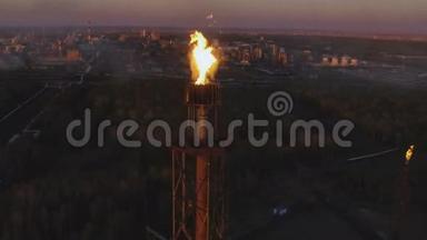 日落时分，一座塔在树林间的炼油厂上挂着火炬。 空中景观