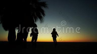 日落背景下的家庭游戏。 孩子们和父亲在海边玩耍的剪影