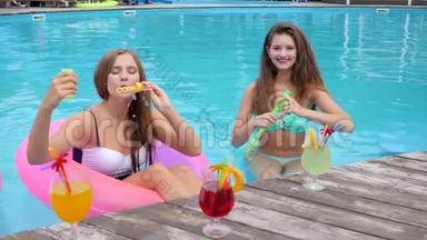 穿着泳衣的女朋友在游泳池里吹肥皂泡，鸡尾酒会，穿着泳衣休息的漂亮女孩
