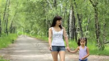 家庭价值观。 年轻的妈妈牵着小女孩的手在公园散步。