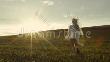 运动的女孩跑到明亮的日落，绿色的草坪和自由的空间周围。 慢动作。 生命的美丽