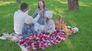 在公园野餐时，一家人坐在草地上，都吃早餐。 有一个带餐的篮子。 新鲜