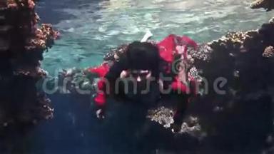 在红海珊瑚的背景下，自由潜水者穿着红色衣服。