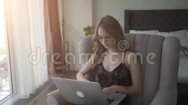 可爱的女人在家里坐在扶手椅上用笔记本电脑工作