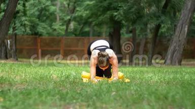 一位身穿运动服的年轻运动员女士在绿色草坪上的公园里躺在地毯上从事健身活动