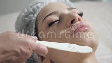 用刮刀泡沫从<strong>面部</strong>取出。 年轻漂亮的女人在美容院接受治疗。 <strong>面部</strong>清洁泡沫