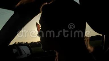 风吹过女孩的剪影和头发在车里。 日落