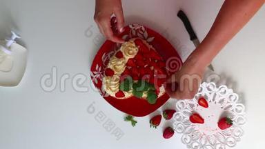 女人用草莓和柠檬香膏装饰饼干。 <strong>碟子</strong>旁边是一个切片草莓。