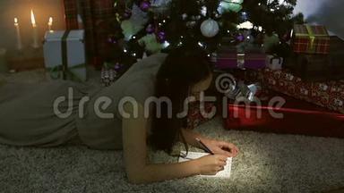 一个穿灰色衣服的小女孩躺在圣诞树附近的地板上，给圣诞老人写了一封信。