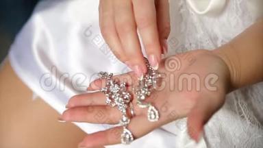 婚礼耳环在新娘手上，新娘`早晨和珠宝配件和装饰概念。 女孩戴耳环