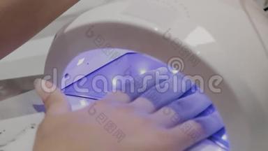 一个年轻的女孩在美甲沙龙的紫外线灯下干指甲油。