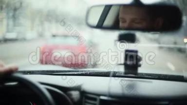 在城市里开车的时候对着镜子微笑的人。 英俊的男人的脸。 前窗上的雨滴。 开车旅行。
