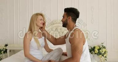 情侣相爱相拥微笑坐床面对面混血男人抚摸女人脸拥抱早间卧室
