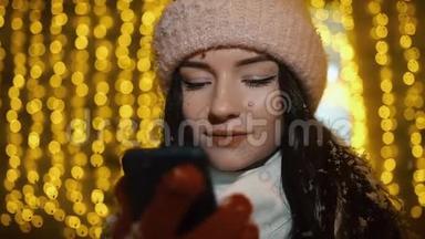 美丽迷人的女孩站在一家装饰有花环的橱窗附近，使用智能<strong>手机</strong>。 新年圣诞<strong>节</strong>
