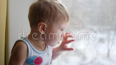 孩子坐在窗台上，看着窗外的雪特写。