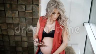 怀孕的<strong>未来</strong>母亲穿着红色衬衫，蓝色牛仔裤和黑色胸罩，坐在窗台上，带着<strong>智</strong>能手机。 青年