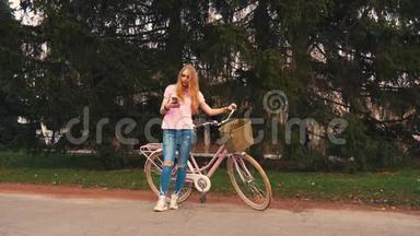 姜红头女孩坐在自行车上，在夏季公园的智能手机上发短信。 穿着粉色衬衫和牛仔裤