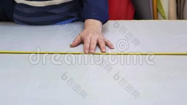 在一家家具厂里，一位年长的妇女正在用一个衬衫为沙发测量和标记一种灰色材料。