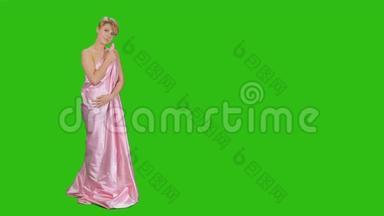 穿着粉红色缎子<strong>床单</strong>的漂亮女孩在绿色背景下摆着相机