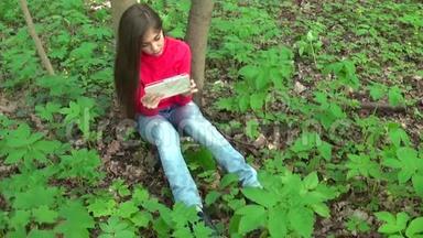 公园里坐在草地上的一个年轻漂亮的女孩，手里拿着平板电脑。静态摄像机的电影。