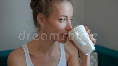 年轻漂亮的女人手里拿着白色的杯子坐在沙发上的家里。