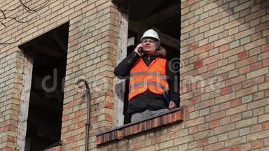工地经理在大楼二楼窗户上用智能手机说话