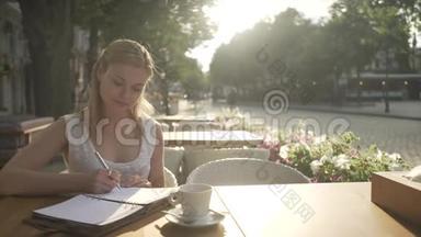 穿着白色裙子的金发少女在咖啡馆外的露台桌上写着个人<strong>日记日记</strong>，看着远方
