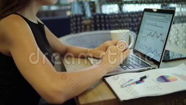 现代建筑师的临时工作日。 一位年轻漂亮的女士，一边拿着笔记本电脑一边端着咖啡杯坐着