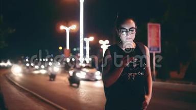 在一个夜晚的城市里，漂亮的女人一边用<strong>手机</strong>在街上行走，在<strong>后台</strong>可以看到