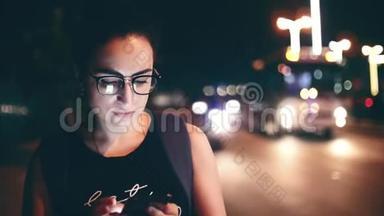 在一个夜晚的城市里，漂亮的女人一边用手机在街上行走，在后台可以看到