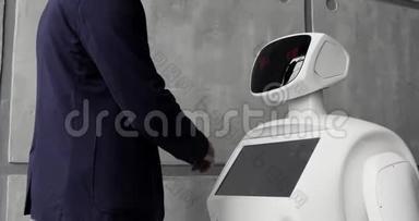 一个时尚的男人与机器人交流，把一只塑料机械手臂按在机器人身上，握手。 控制系统