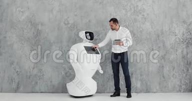 一个时尚的男人与机器人交流，把一只塑料<strong>机械手臂</strong>按在机器人身上，握手。 控制系统