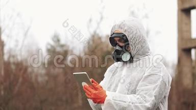 穿着生物危险服和防毒面具的人在被污染的土地上的平板电脑上记笔记
