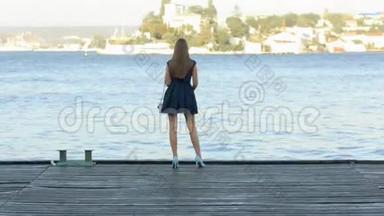 美丽的女孩，一头长发，穿着连衣裙，站在木墩上，望着大海