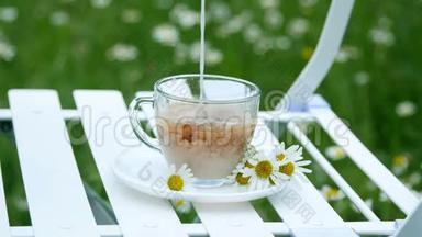特写，减速.. 在一个用雏菊装饰的白色<strong>茶托</strong>上，有一个装有茶的玻璃杯。 牛奶倒进去