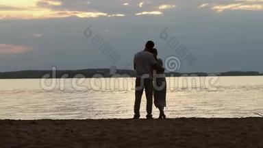 日落时分<strong>情人</strong>的<strong>剪影</strong>。 年轻漂亮的夫妇拥抱在湖岸上