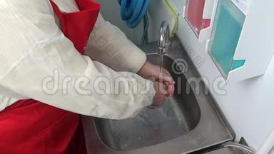穿红色围裙的女工在水龙头下洗手.