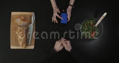 厨房桌子上的俯视图。 手拿着蓝屏的手机..