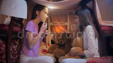 两个姐妹坐在卧室的毯子下面，用手电筒<strong>讲故事</strong>